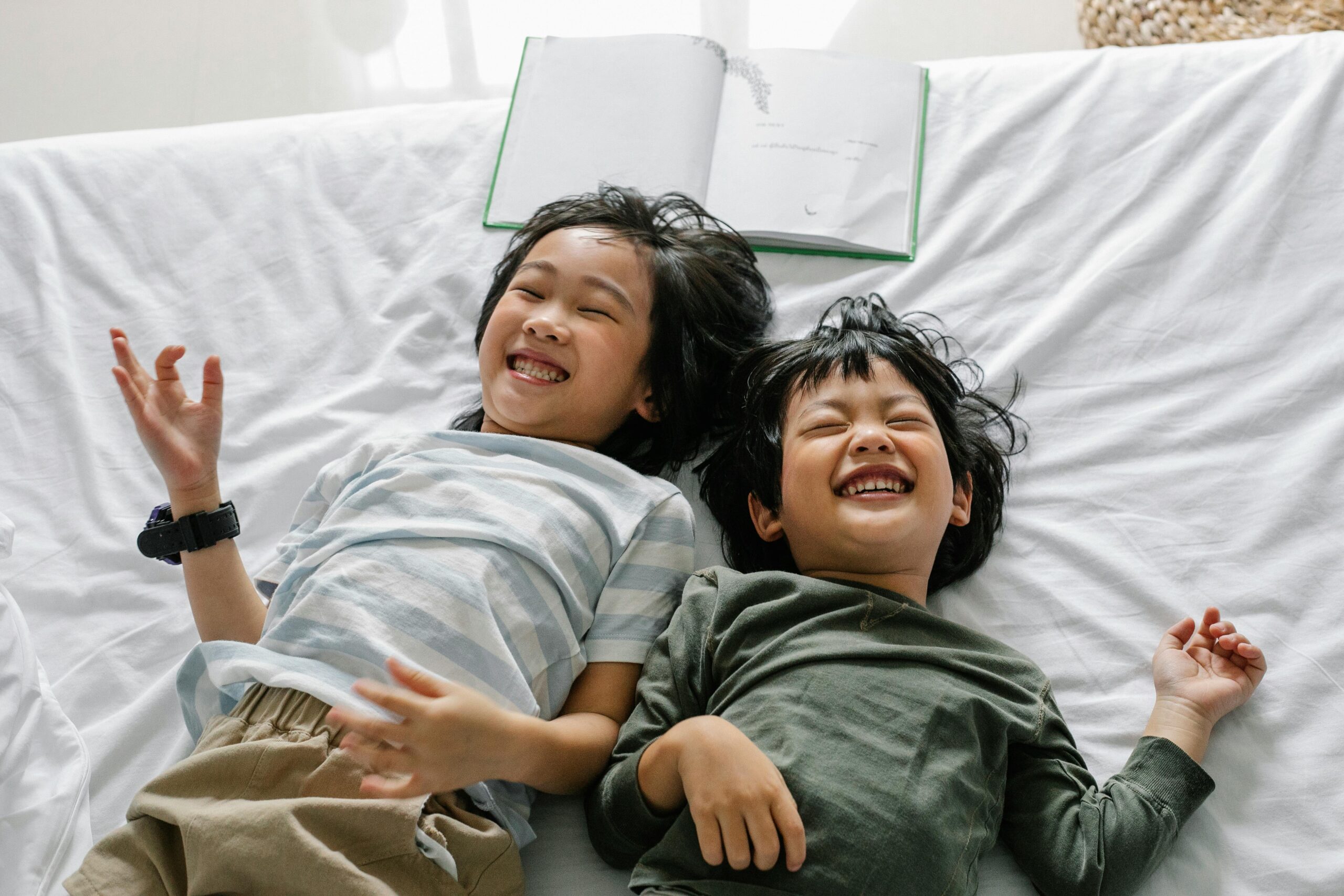 Two cheerful children laughing together while relaxing indoors on a cozy bed. Perfect sibling moments.